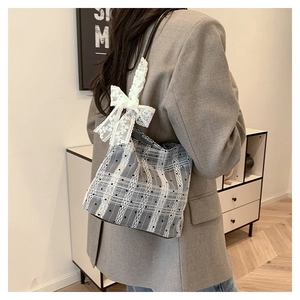 Detail of grey plaid shoulder bag featuring white lace trim and large decorative bow