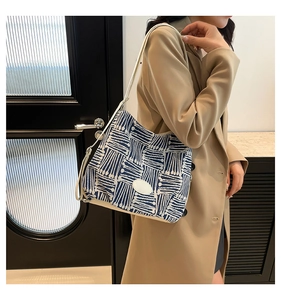 Détail d'un sac cabas tissé bleu et blanc avec des lanières en cuir blanc sur un mannequin