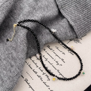 Elegant beaded necklace with black crystals and white flower charms on a sweater background