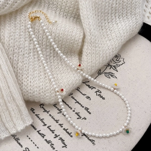 Elegant white pearl necklace with colorful floral pendants on soft knit background