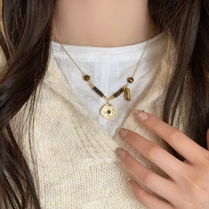 Tiger eye stone necklace with gold relief pendant worn over a white knit sweater