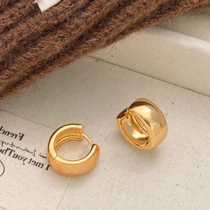 Minimalist round geometric huggie earrings with polished gold finish on soft fabric