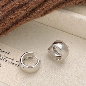 Close-up of minimalist polished silver hoop earrings on a textured fabric background