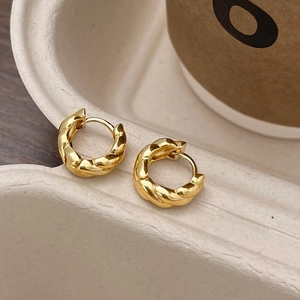 Détail des boucles d'oreilles créoles torsadées dorées avec texture polie et fermoir boucle