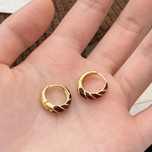 Detailed macro view of red enamel and gold-plated hoop earrings with spiral twisted texture