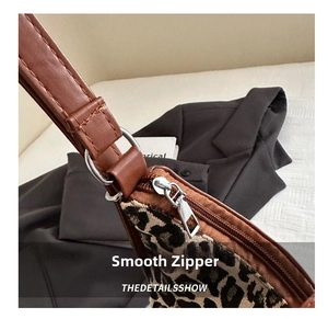 Close-up of the smooth metal zipper and brown leather trim on the leopard print tote bag