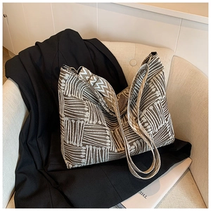 Dettaglio borsa shopper a trama geometrica con tracolla larga su una sedia