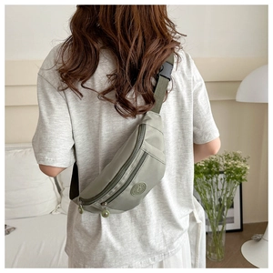 Sac banane en nylon vert sauge porté en bandoulière dans un décor de style de vie décontracté