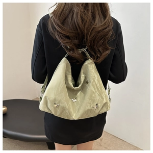 Détail du sac hobo vert clair avec papillons argentés sur tissu plissé brillant