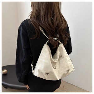Grand sac cabas blanc avec breloques papillon en métal porté sur l'épaule