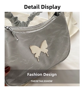 Detail of light grey crescent bag featuring wrinkled fabric and silver butterfly logo