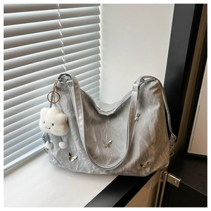 Détail du sac cabas argenté avec papillons et charm nuage en peluche sur un rebord