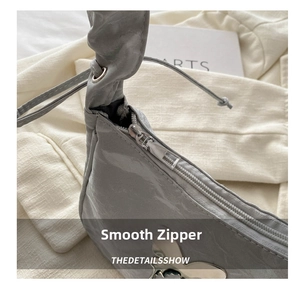 Detailed close-up of grey patent leather shoulder bag featuring smooth metal zipper and logo