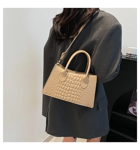 Detail der beigen Handtasche mit Krokodilmuster und Riemen an einem grauen Blazer-Model