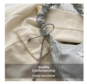 Detail of grey cloud bag featuring pleated straps and a metallic heart-shaped buckle
