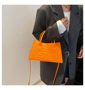 Detail der orangefarbenen Handtasche mit Krokodilprägung und festem Tragegriff