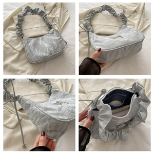 Detail of silver crescent hobo bag featuring ruffled handle and metallic bow ornament