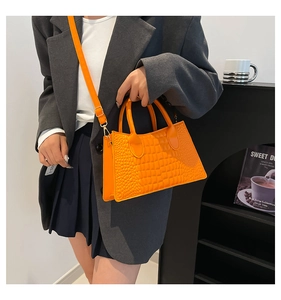 Detail der leuchtend orangefarbenen Handtasche mit Krokodilmuster und Goldbeschlägen