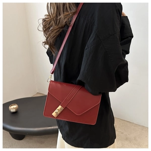 Chic red vintage crossbody bag with gold lock closure shown on a model in a minimalist setting