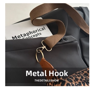 Detail of golden metal hook and brown leather trim on leopard print tote bag