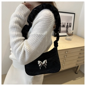 Detail of black pleated cloud bag featuring silver butterfly charm and ruffled shoulder strap