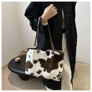 Detail of cow print plush tote bag with dark brown faux leather handle and metal rings
