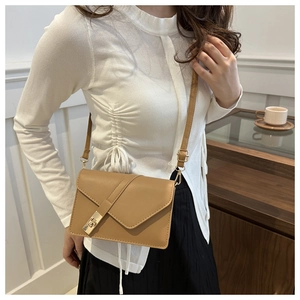 Close-up of a camel leather crossbody bag with a golden metal lock on a model