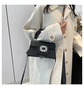 Detail of black crocodile texture handbag with crystal buckle on beige trench coat