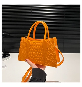 Detailansicht der hellorangen Handtasche mit Krokodilprägung und zylindrischen Griffen