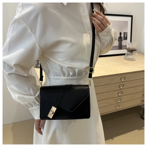 Detail of black leather envelope crossbody bag with gold rectangular lock on strap
