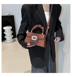 Brown lizard-embossed handbag with rhinestone buckle and pleated handle shown on model