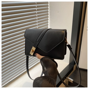 Detail of black leather crossbody bag with geometric envelope flap and gold twist lock