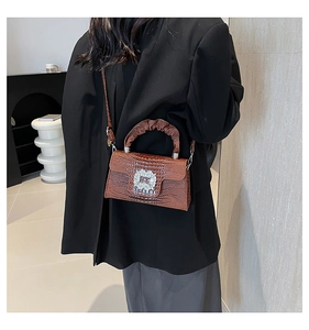 Detail of a brown faux crocodile leather crossbody bag with a large rhinestone square buckle