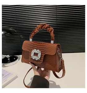 Detail of glossy crocodile pattern leather handbag with crystal buckle and ruffled handle