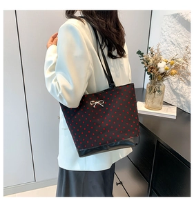 Detail of black tote bag with red heart prints and silver bow buckle on white blazer