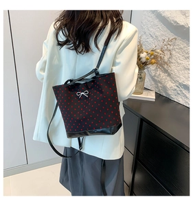Detail view of black canvas tote bag with red heart pattern and silver bow on model