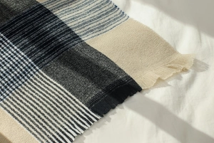 Close-up of thick woven blue and beige plaid scarf with fringe detail in soft sunlight