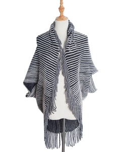 Detail of black and white striped knit poncho featuring elegant long fringe trim and texture