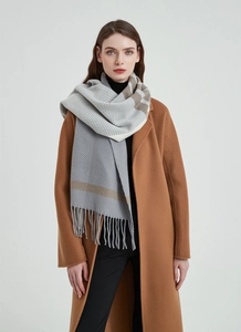 Detail view of a gray plaid scarf with long tassels paired with a wool camel coat
