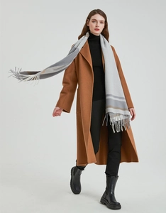 Full view of a grey plaid tassel scarf styled with a long brown wool coat and boots