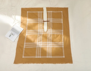 Détail du châle à carreaux jaune avec boucle en cuir et franges sur une maille douce