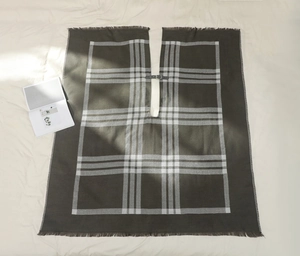 Détail d'un poncho écossais olive avec boucle en cuir marron et bordure à franges