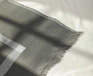 Gros plan du motif à chevrons gris et bords à franges sur un châle en cachemire doux