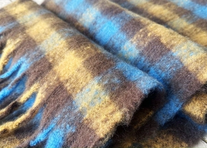 Dettaglio del tessuto della sciarpa a quadri con trama in mohair blu e morbide nappe sui bordi