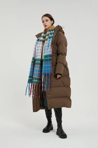Detail view of long brown puffer coat paired with a colorful rainbow plaid fringed scarf