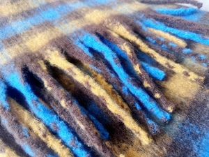Dettaglio della sciarpa in mohair a quadri blu e marroni con texture morbida e nappe