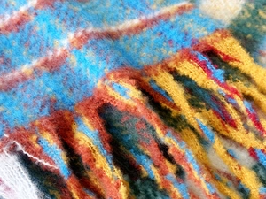Detailed close-up of thick rainbow plaid scarf with coarse fringe and knit texture