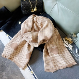 Detail of knit scarf with heart pattern, plaid texture, and fringe on a neutral background