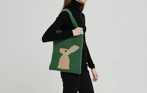 Dettaglio della borsa shopper in maglia verde con motivo a coniglio beige su modella
