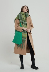Dettaglio borsa in maglia verde e sciarpa a righe con frange su cappotto color cammello